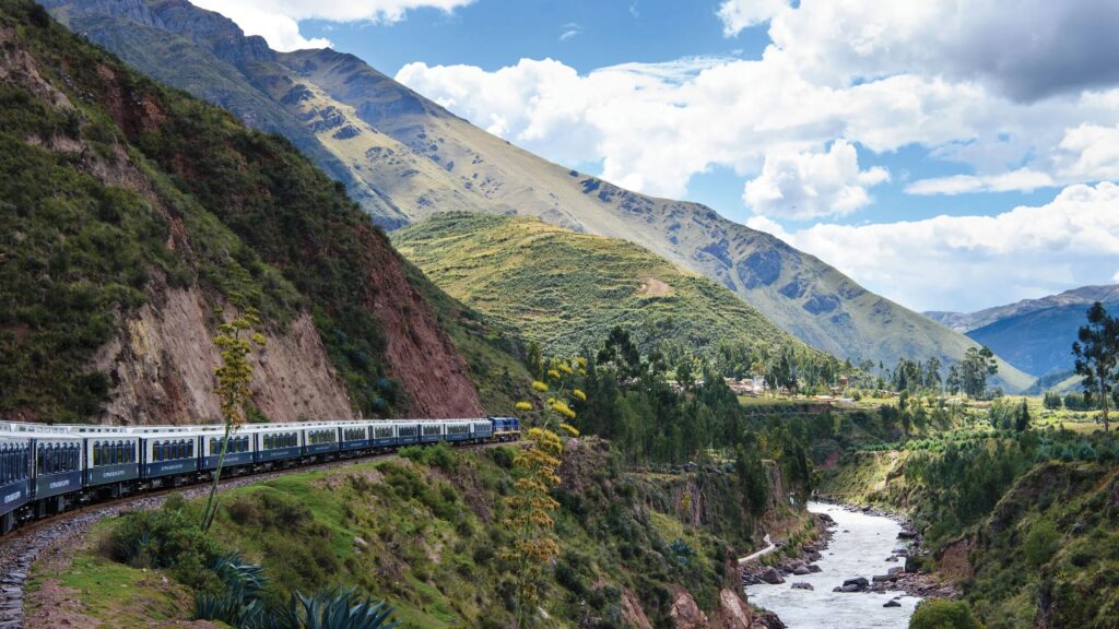 The Belmond Andean Explorer train traveling through expansive green landscapes in Peru, with a river flowing nearby