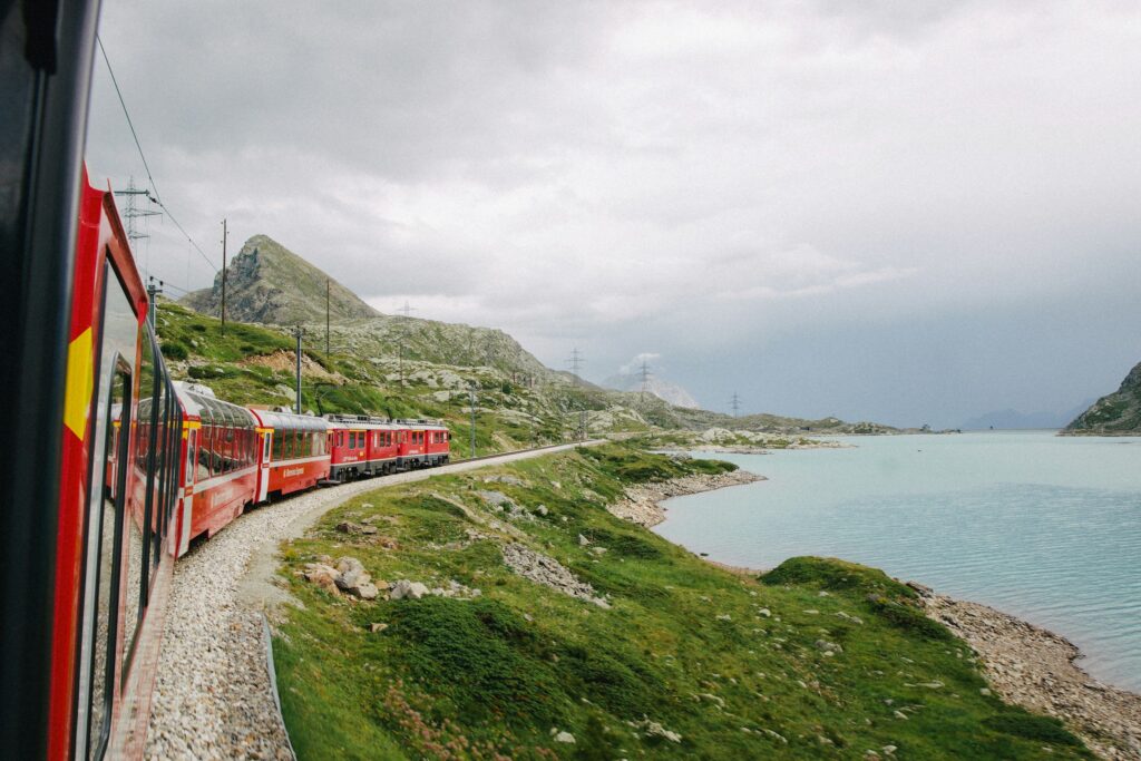 Glacier Express train traveling along a serene lake surrounded by lush green mountains in Switzerland